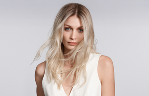white woman with long blonde hair, which stands in front of a clean grey background looking into the camera