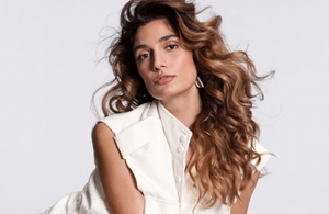 a white woman with blonde long hair looking straight into the camera in front of a grey background
