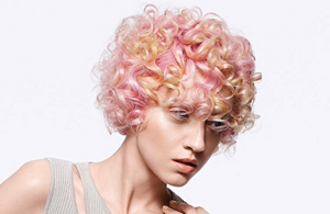 Women with short, curly and pink hair in front bright background.