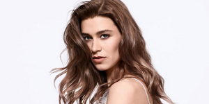 Serious looking woman with brown wavy hair and bright background