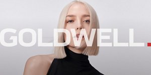 Eine Frau mit blondem, glattem Haar verwendet Goldwell-Elumen-Haarfärbeprodukte auf grauem Hintergrund.