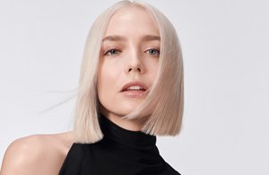 A woman with blonde straight hair used goldwell elumen dying products on a grey background.