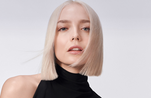 A woman with blonde straight hair used goldwell elumen dyeing products on a grey background.