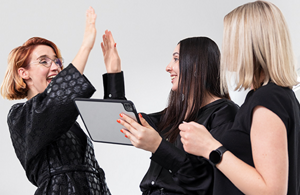 3 stylists with a tablet smiling and high-fiving each other