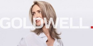 Woman with grey hair smiling and glancing at her right on light grey background with Goldwell logo in the center
