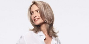 Woman with grey hair smiling and glancing at her right on light grey background