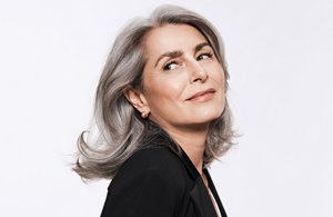 Woman with grey hair smiling glancing at her left on a light grey squared background .