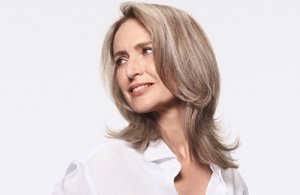 Woman with grey hair smiling and glancing at her right on light grey background and square frame.