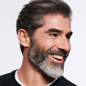 Man with dark grey hair and beard glancing on his left and smiling.