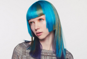 Woman with dark wavy hair wearing a white blouse in front of bright background