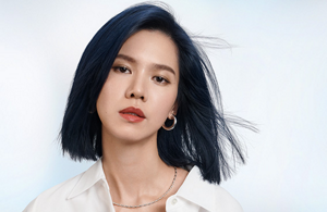 Woman with dark wavy hair wearing a white blouse in front of bright background