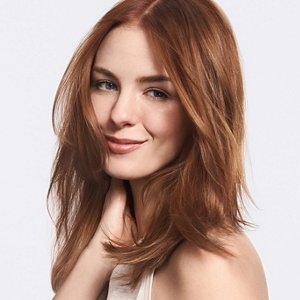 A smiling woman with long brown hair holding her neck