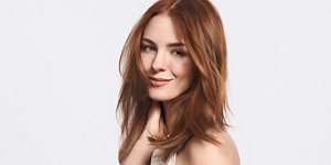 A smiling woman with long brown hair holding her neck