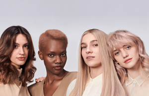 four diverse woman with different hair colors and lenghts, which stand side by side and close to each other looking into the camera while standing in front of a clean grey background