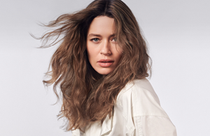 A woman with brown curly hair, who used products from the muted Goldwell collection, stands in front of a grey background.