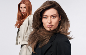 Two women with brown and red hair, using products from the Goldwell Muted Collection, standing in front of a grey background.