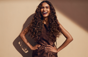 Woman with dark wavy hair wearing a white blouse in front of bright background