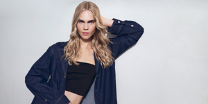 Woman with red hair glancing at the camera on light grey background with the Topchic 50 years logo in the right top corner.