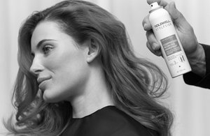 a woman with long hair using goldwell hair spray in black and white