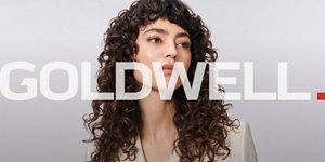 a woman with brown curly hair used goldwell texture dimensions perm product line on a grey background