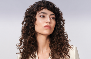 a woman with brown curly hair used goldwell texture dimensions perm product line on a grey background
