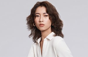 a woman with brown curly hair used goldwell texture dimensions perm product line on a grey background looking into the camera