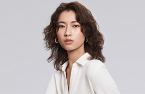 white woman with long blonde hair, which stands in front of a clean grey background looking into the camera