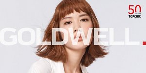 Woman with brown hair glancing at the camera on light grey background with the Topchic 50 years logo in the right top corner and the Goldwell logo in the front.