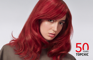 Woman with red hair glancing at the camera on light grey background with the Topchic 50 years logo in the right bottom corner.