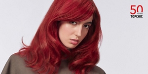 Woman with red hair glancing at the camera on light grey background with the Topchic 50 years logo in the right top corner.