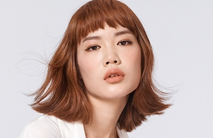 Woman with brown hair glancing at the camera on light grey background.