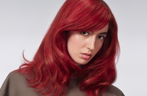 Woman with red hair glancing at the camera on light grey background.