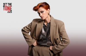 Woman with dark wavy hair wearing a white blouse in front of bright background