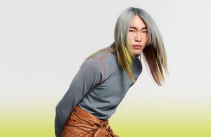 Woman with dark wavy hair wearing a white blouse in front of bright background