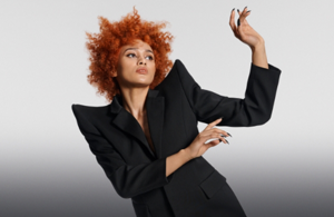 white woman with long blonde hair, which stands in front of a clean grey background looking into the camera