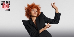 white woman with long blonde hair, which stands in front of a clean grey background looking into the camera