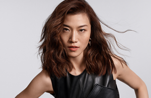 white woman with long blonde hair, which stands in front of a clean grey background looking into the camera