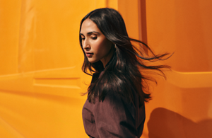  In front of a bright orange backdrop, a model shows of the sleek shine of her flowing dark hair, created thanks to Goldwell's range of products
