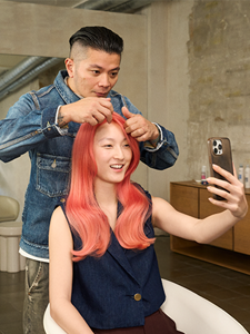  Peter Wu, a Goldwell Global Stylist, points out the vibrance and depth of color in his smiling model's pink hair as she uses her phone as a mirror to look at the finished results. Thanks to Goldwell's product range the model's hair is vibrant and brilliant
