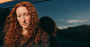 A model stands in front of a dark car in a black top which helps to highlight the vibrance of her curly orange hair thanks to Goldwell's hair range.