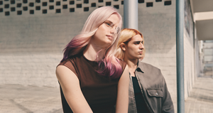An image of a woman with pale pink mid-length hair and ombre at the ends to purple, next to a man with orange-blonde shoulder length hair. Showcasing the Goldwell Velvet Gradients campaign.