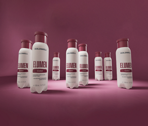 Goldwell Elumen groupshot showing multiple white Elumen Color bottles displayed together on a burgundy pink studio background.