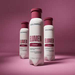 Goldwell Elumen transformation packshot showing three white Elumen Color bottles with burgundy caps arranged on a burgundy pink studio background.