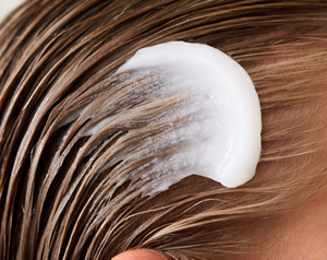 Close-up image of a model applying Goldwell's Dualsenses Bond Pro 60 Sec Treatment to wet hair, demonstrating the product's creamy texture and application method for strengthening weak and fragile hair