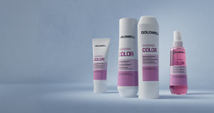 Goldwell Dualsenses Color haircare range displayed as white and pink shampoo, conditioner, treatment and spray products on a soft blue studio background.
