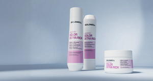 Goldwell Dualsenses Color Extra Rich haircare range displayed as white and pink shampoo, conditioner and treatment products on a soft blue studio background.