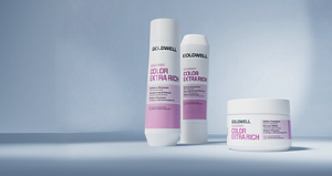 Goldwell Dualsenses Color Extra Rich haircare range displayed as white and pink shampoo, conditioner and treatment products on a soft blue studio background.