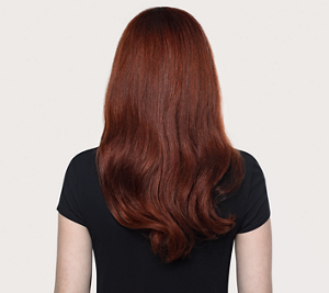 Goldwell Dualsenses Color Extra Rich after image showing a person from behind with smoother, shinier long auburn hair and a black top against a neutral studio background.