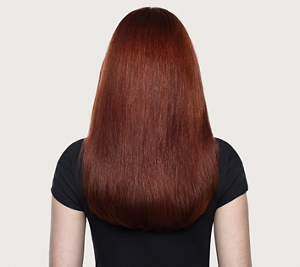 Goldwell Dualsenses Color Extra Rich before image showing a person from behind with long auburn hair and a black top against a neutral studio background.