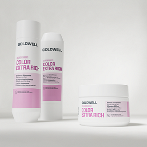Goldwell Dualsenses Color Extra Rich haircare products shown as shampoo, conditioner and treatment jar in white and pink packaging on a soft light grey studio background.